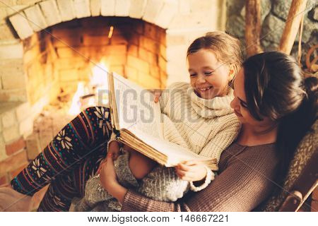 Mom with child reading book and relaxing by the fire place some cold evening, winter weekends, cozy scene