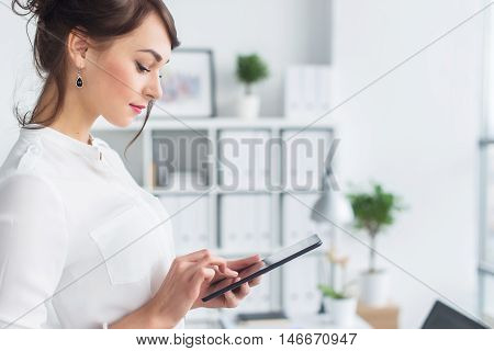 Portrait of an office manager holding her tablet, typing, using wi-fi internet and applications touching the pda screen