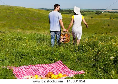Back view of young couple going home arter picnic, they left fruits and blanket on the grass