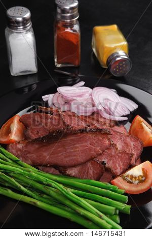 business lunch fresh roast beef meat slices on black plate wotj cutlery asparagus boiled broccoli rye bun on wooden table