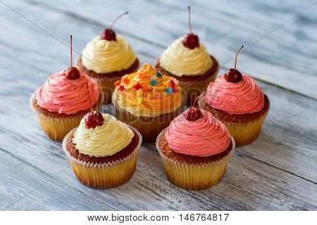 Colorful cupcakes with cherries. Small desserts on wooden surface. Soft dough and frosting. Tasty sweet treats.
