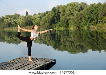Young beautiful woman engaged in yoga on the river bank, Asana on balance Nataraja asana
