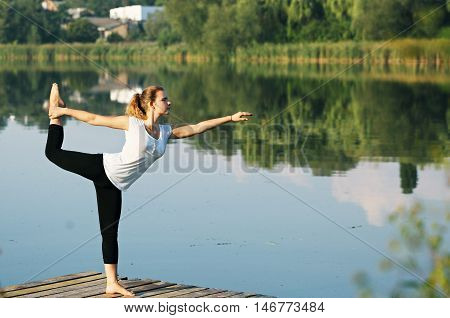 Young beautiful woman engaged in yoga on the river bank, Asana on balance Nataraja asana