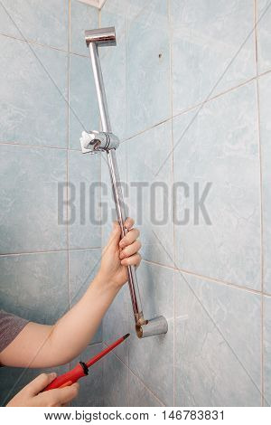 Close-up hands uninstalling the broken vertical height adjustable shower bar slider rail holder using red phillips screwdriver.
