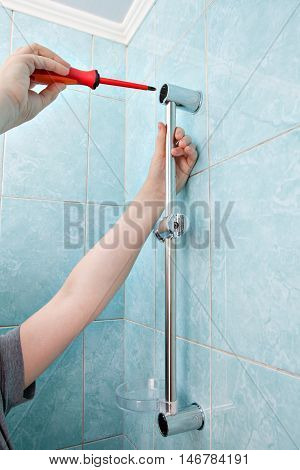 Plumbing repairs in bathroom close-up hands plumber tighten screw holder for shower using screwdriver.