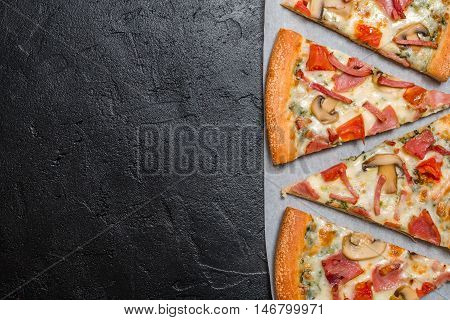 Cut into slices delicious fresh pizza with mushrooms and ham on a dark background. Top view . Pizza on the black table.
