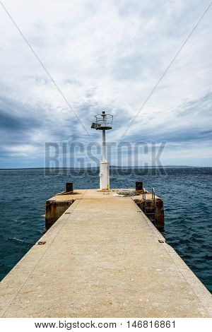 Old Pier With A Lighthouse Beacon And Calm Sea.
