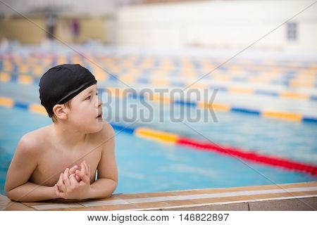 Cute little kid boy having rest after swimming in the sport swimming pool. Training for competition. Sport activities for children.