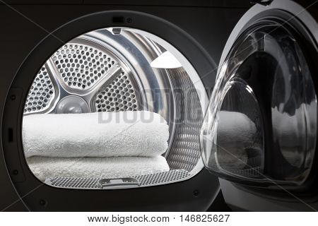 Stacked clean white towels inside washing machine drum. Clean concept. Laundry. Closeup of open washing machine.