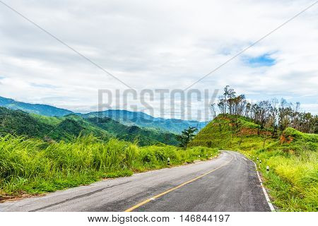 Empty curved asphalt road on green forest on mountain with cloudy sky.