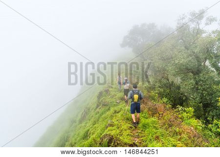 Foggy clouds cover hikers team on top of green mountain ridge.