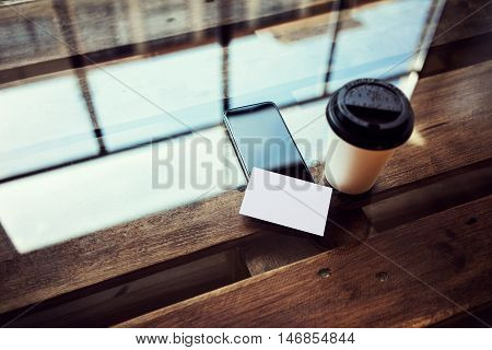 One Blank White Paper Business Card Mockup Wood Table.Take Away Coffee Cup Coworking Studio.Modern Phone Work Office Reflection Glass Background.Mock Up Objects Ready Private Message.Horizontal Photo