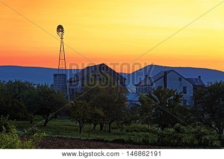 A beautiful sunrise on a rustic Amish farmstead with a windmill in Pennsylvania, USA.