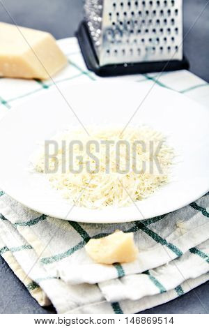 Piece and grated parmigiano reggiano or parmesan cheese on white plate on checkered napkin . Grated parmesan uses in pasta dishes, soups, risottos and grated over salads.