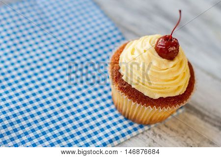 Frosted cupcake on blue napkin. Dessert with icing and cherry. Tasty pastry in diner. New sweet dish in menu.