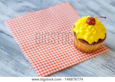 Yellow cupcake on a napkin. Red cherry on icing. Dessert served at the diner. How to lift mood.