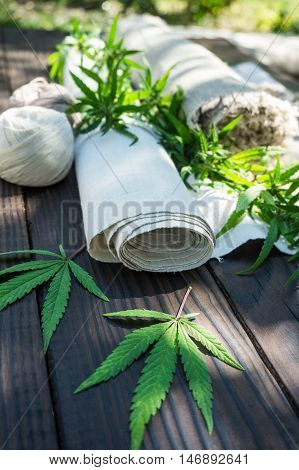 Leaves of cannabis and hemp cloth rollon the dark wooden surface. Hemp products. Agricultural technical culture