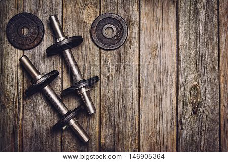 Old iron dumbbells or exercise weights with extra plates on an old wooden deck, floor or table. Image taken from above, top view. A lot of copy space around product