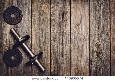 Old iron dumbbells or exercise weights with extra plates on an old wooden deck, floor or table. Image taken from above, top view. A lot of copy space around product