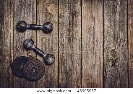 Old iron dumbbells or exercise weights with extra plates on an old wooden deck, floor or table. Image taken from above, top view. A lot of copy space around product