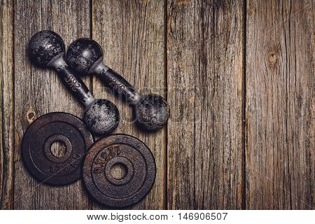 Old iron dumbbells or exercise weights with extra plates on an old wooden deck, floor or table. Image taken from above, top view. A lot of copy space around product