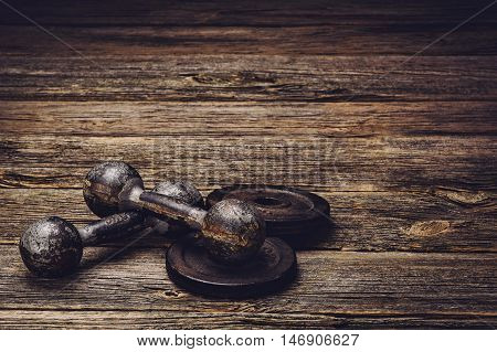 Old iron dumbbells or exercise weights with extra plates on an old wooden deck, floor or table. Image taken from above, low angle . A lot of copy space around product