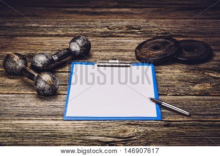 Old iron dumbbells or exercise weights with extra plates on an old wooden deck, floor or table. Image taken from above, low angle or top view. A lot of copy space around product