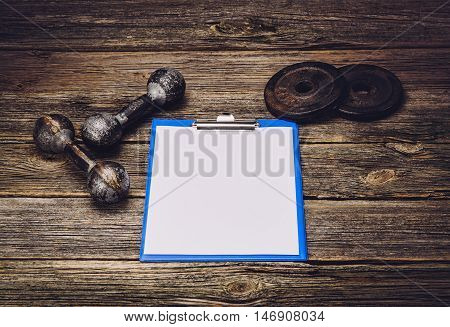 Old iron dumbbells or exercise weights with extra plates on an old wooden deck, floor or table. Image taken from above, low angle . A lot of copy space around product