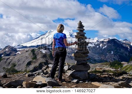Woaman on mountain top with stone cairn against snow capped Mount Baker. Cascade Mountains. Mount Baker National Forest. WA, USA.