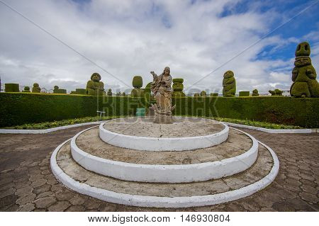 TULCAN, ECUADOR - JULY 3, 2016: statue of an angel standing over a demon in the center of the cemetery surrounded by plants sculptures.