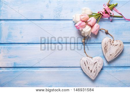 White and pink spring tulips and two decorative hearts on blue wooden background. Pastel colors. Shubby chic. Selective focus. Place for text.