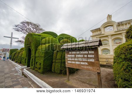 TULCAN, ECUADOR - JULY 3, 2016: some plants sculptures at the entrance of the cemetery next to a wood sign with a phrase on it.
