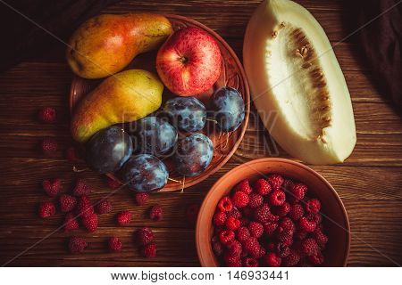 Fresh autumn fruits lie on a wooden table. Harvest of fresh fruit on the table. Fresh apples pears plums raspberries melon on the table.