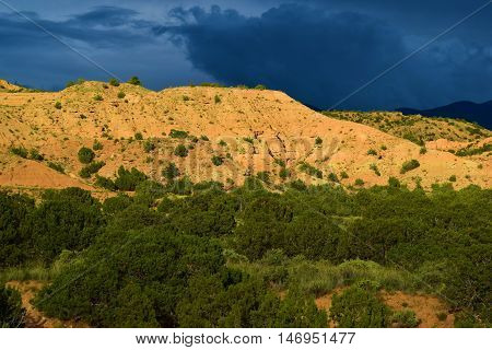 Mesa surrounded by a Pinon and Juniper Woodland with storm clouds beyond taken in rural Northern New Mexico