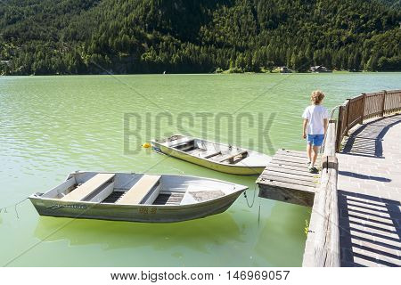 ALLEGHE,ITALY-AUGUST 22,2016:Children stroll near two moored boats on Lake of Alleghe in the Italian's Dolomite.