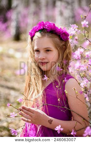 Portrait Of Child With A Long Blond Hair Stands Among The Ledum And Birch In A Pink Dress And Smilin