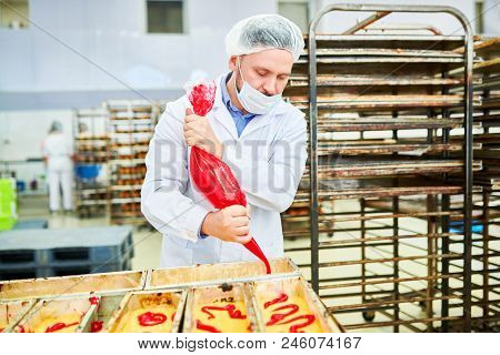 Concentrated Confectionery Factory Worker In White Coat Squeezing Red Cream From Icing Bag.