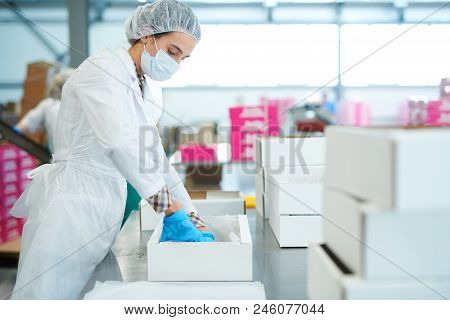 Side View Of Confectionery Factory Worker In White Coat Putting Baking Parchment Into Empty Paper Bo