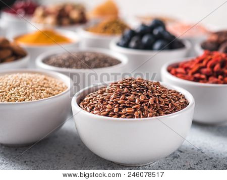 Flax Sseds In Small White Bowl And Other Superfoods On Background Over Gray Concrete Background. Sel
