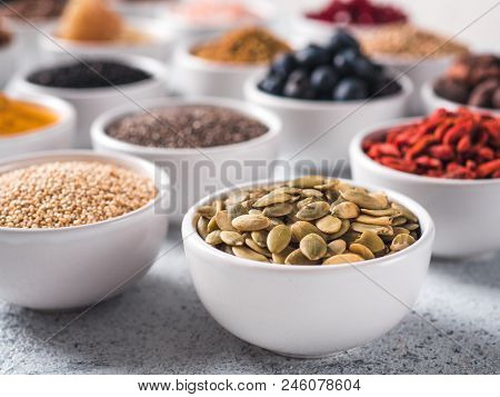 Raw Pepitas Or Pumpkin Seeds In Small White Bowl And Other Superfoods On Background. Selective Focus