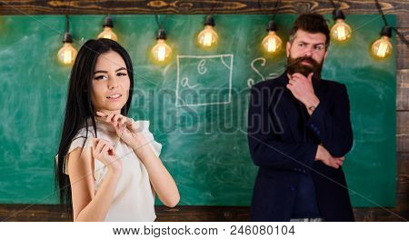 Man With Beard And Young Lady Teacher Stand In Classroom, Chalkboard On Background. Lady Teacher And