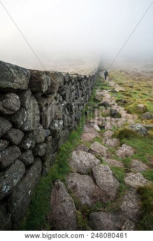 A View Down Slieve Donard Wall Towards A Man Walking Into Low Lying Cloud.
