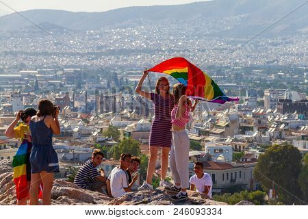 Girls Holding Flag On Athens Pride 2018 Day Being Photographed By Their Friends On A Rock Accross Th