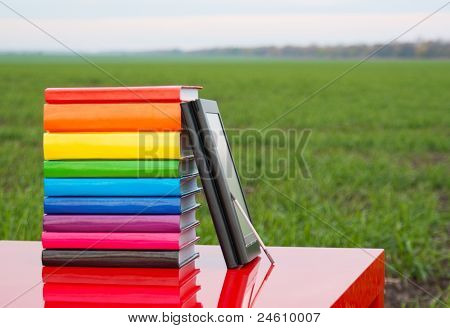 Pile de livres colorés et de lecteur de livre électronique à l'extérieur
