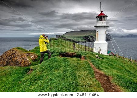photographer with yellow raincoat take a picture of lighthouse in mykinos faroe islands