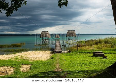 Hammocks On Dock Along The Grass Covered Lake Shore With Dark Blue Cloudscape And Sunshine, El Remat