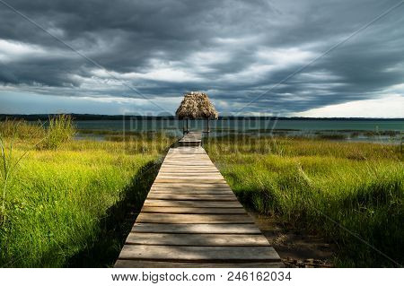 Dramatic Clouds Behind Hut On A Dock Along The Lake Shore With Dark Blue Cloudscape And Sunshine, El