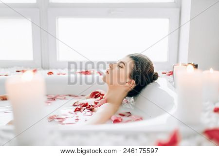 Woman sleeps in the bath with foam, rose petals