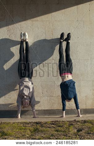Two Young Women Acrobat Doing Handstand On The Wall With Cityscape On Background, Close Up