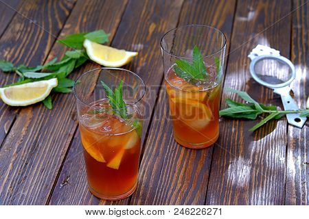 Cool Drink, Cold Black Tea With Lemon, Mint And Ice In Tall Glasses On A Wooden Background. Summer C